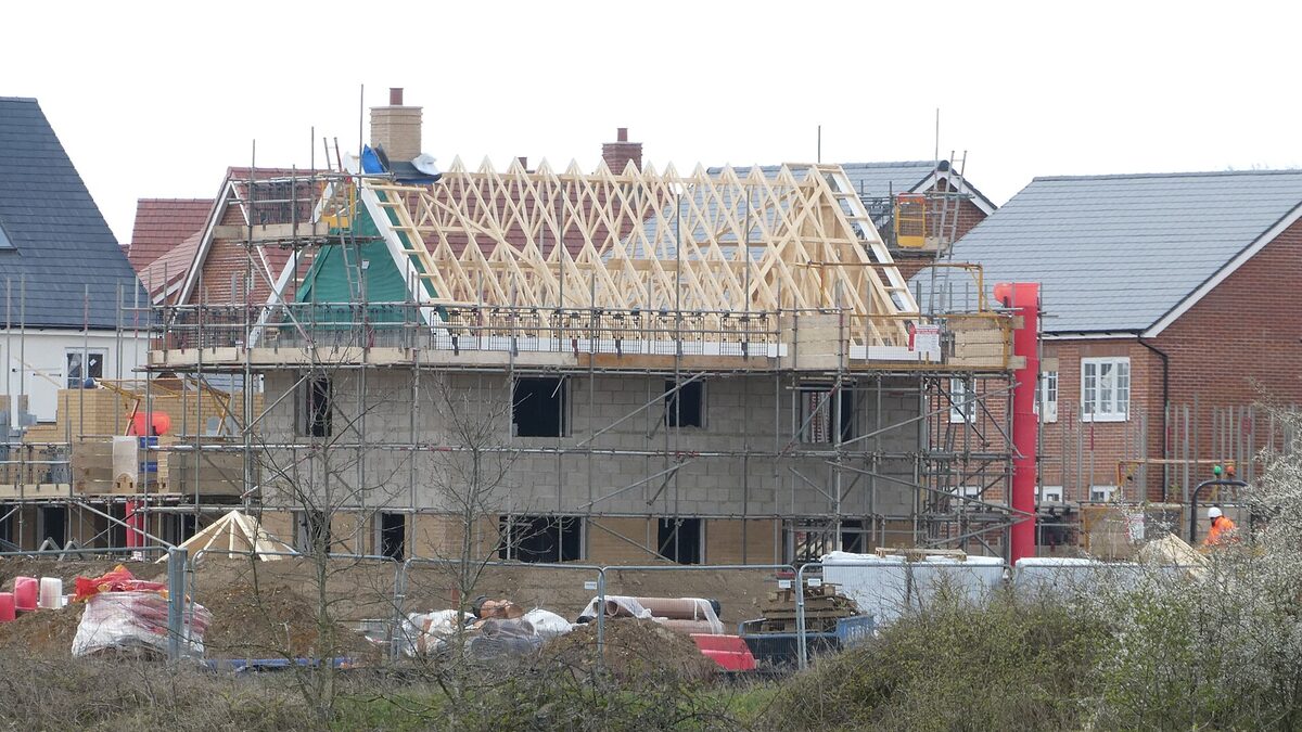 A house part-built on site, wrapped in scaffolding with roof trusses and block walls still open