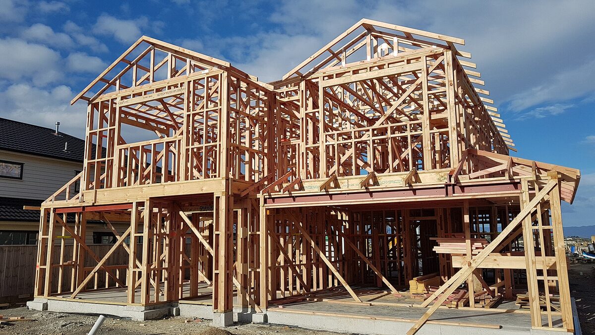 A timber-frame house part-built on a New Zealand site, roof trusses and wall framing up, waiting for its windows