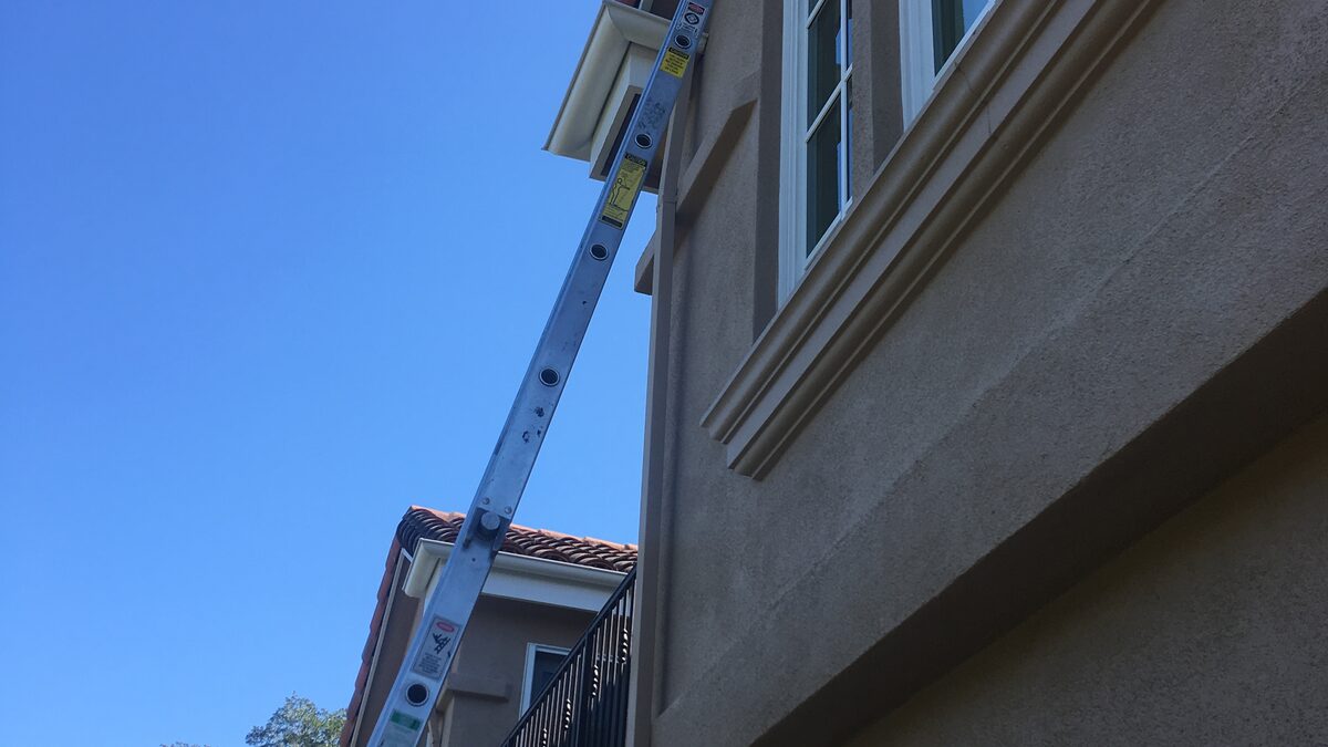 An aluminium extension ladder leaning up the rendered wall of a house to reach the upper windows